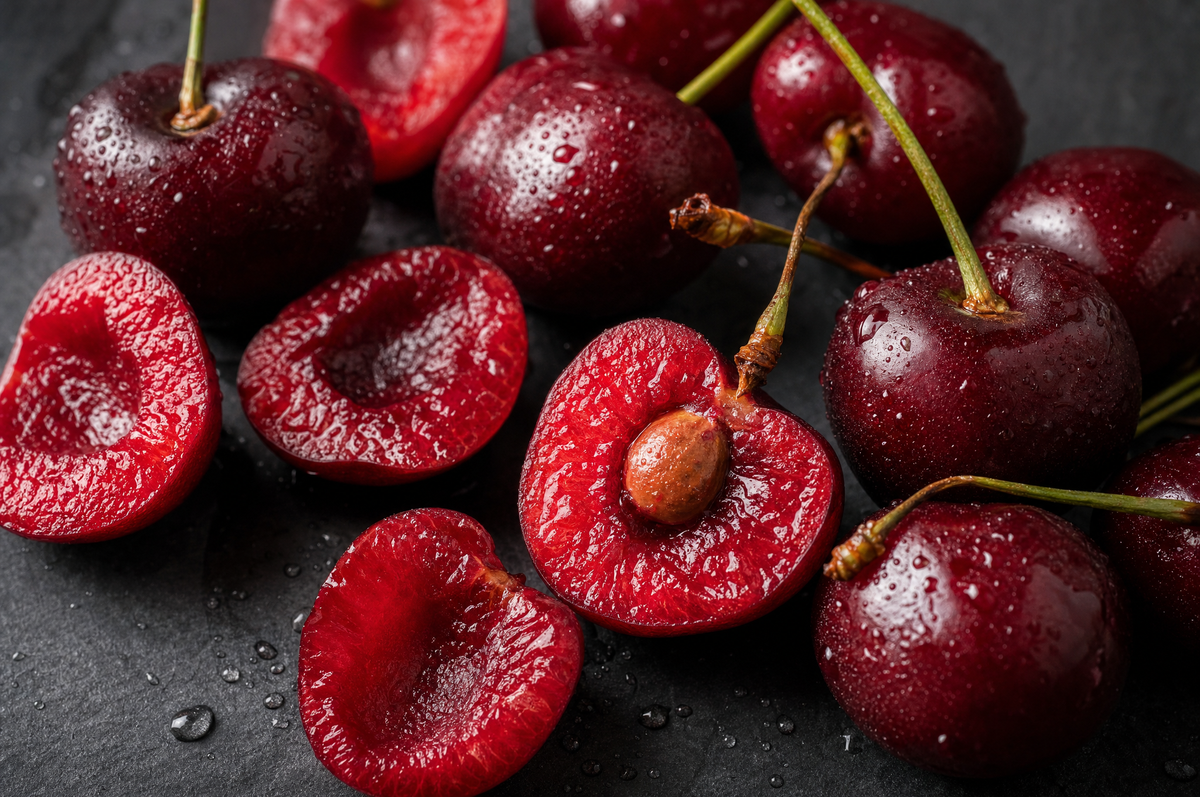 Macro close-up of fresh ripe tart cherries, several halved to show the flesh.