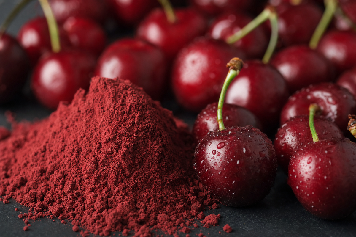 Macro close-up of deep red tart cherry powder beside fresh tart cherries.